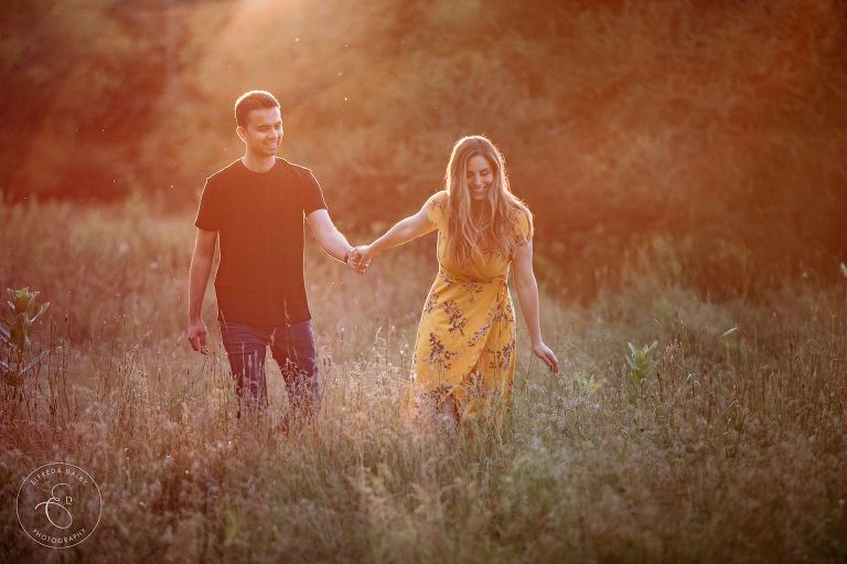 Couple waling through grass at sunset