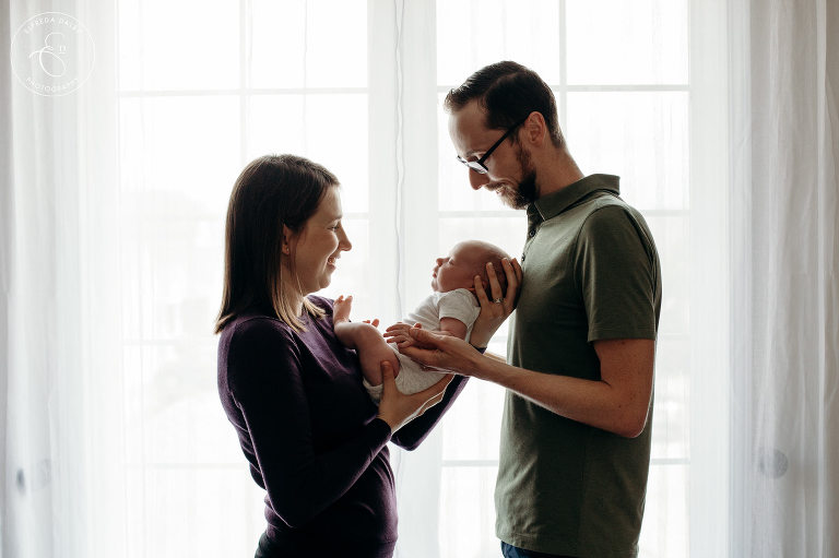 Mom and Dad holding newborn baby in front of the window