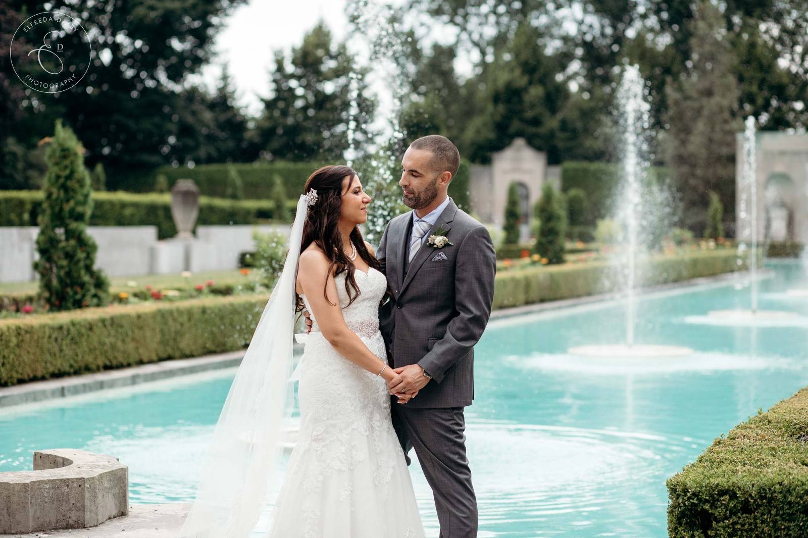 Bride and Groom stand in front of the fountain at Parkwood Estate