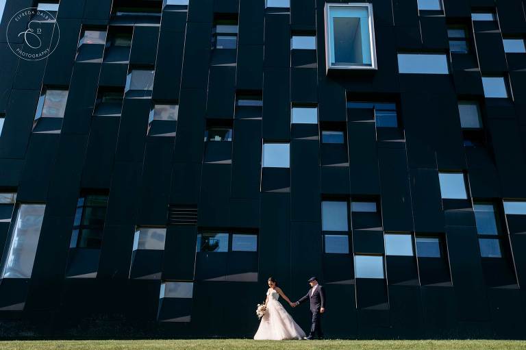 Bride and Groom walk in front of a blue building