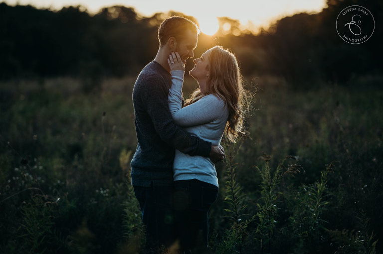 Romantic moment between engaged couple in a field during sunset with golden light