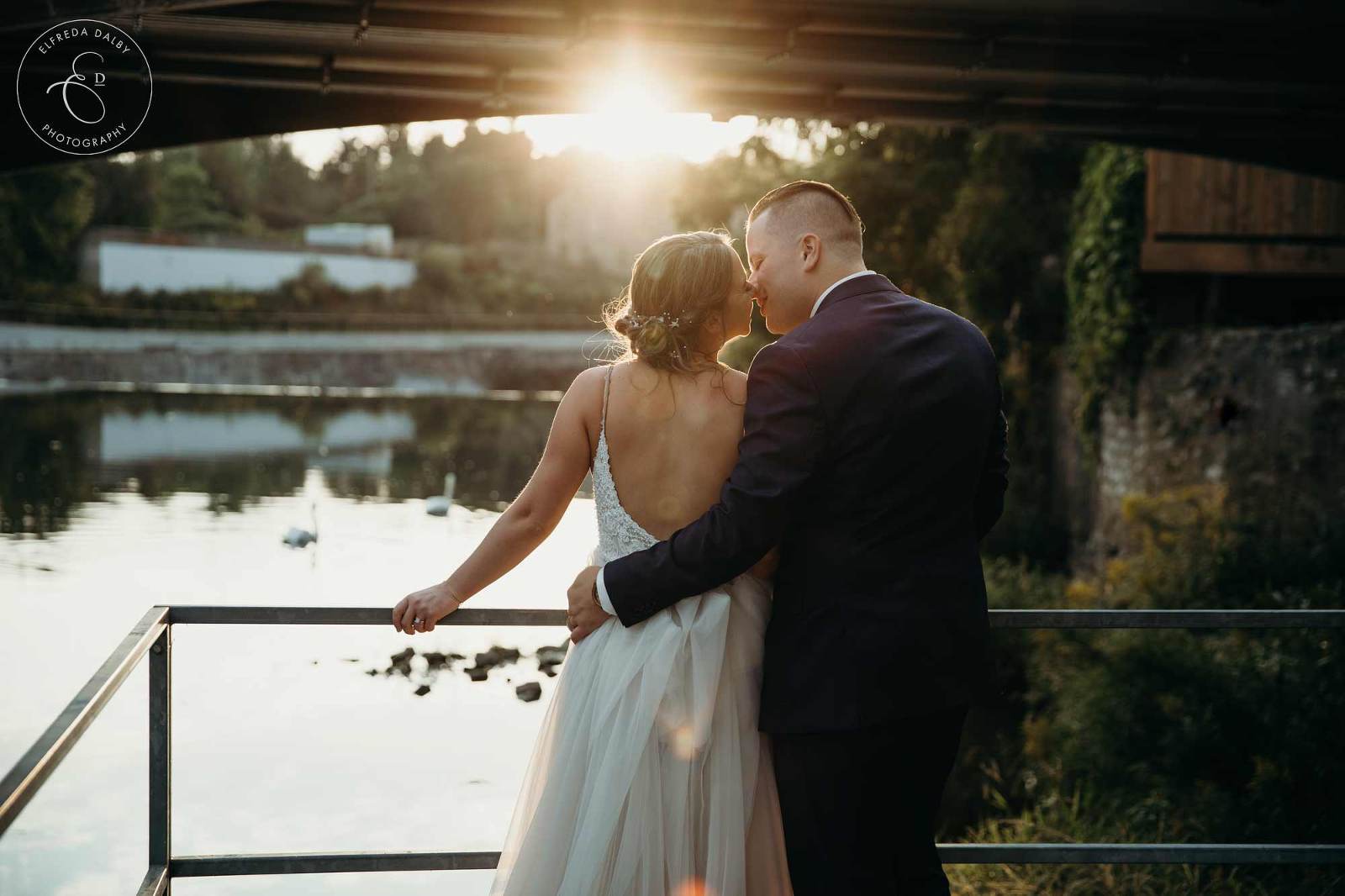 Bride and Groom kiss by the water during golden hour at Elora Mill