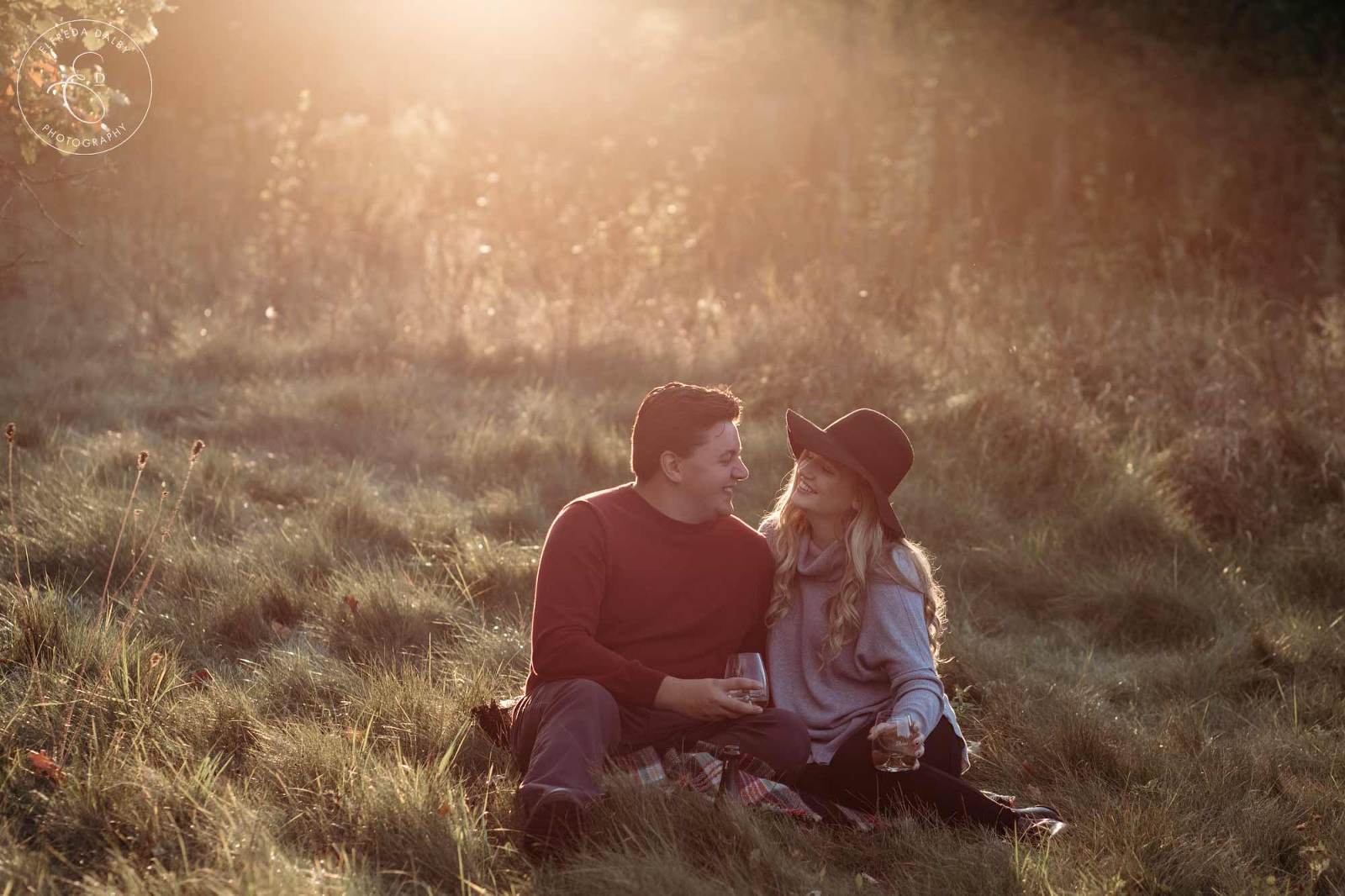 Couple sitting in a field and enjoy champagne during golden hour