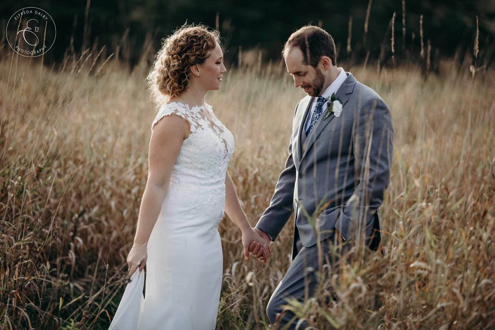 Wedding couple standing in tall grass during sunset