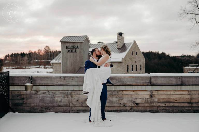 Groom holding bride while kissing on the terrace at Elora Mill