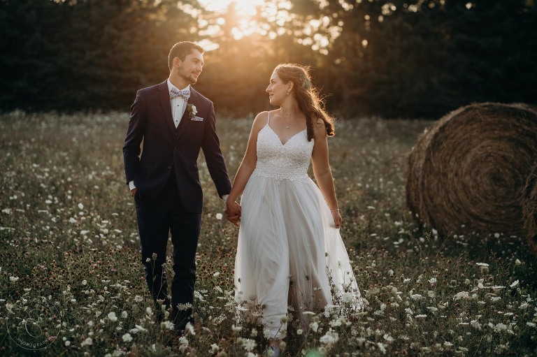 Bride and groom walking through a field during golden hour