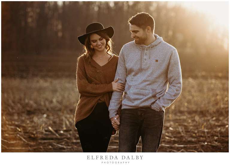 Engaged couple walking over a field during golden hour