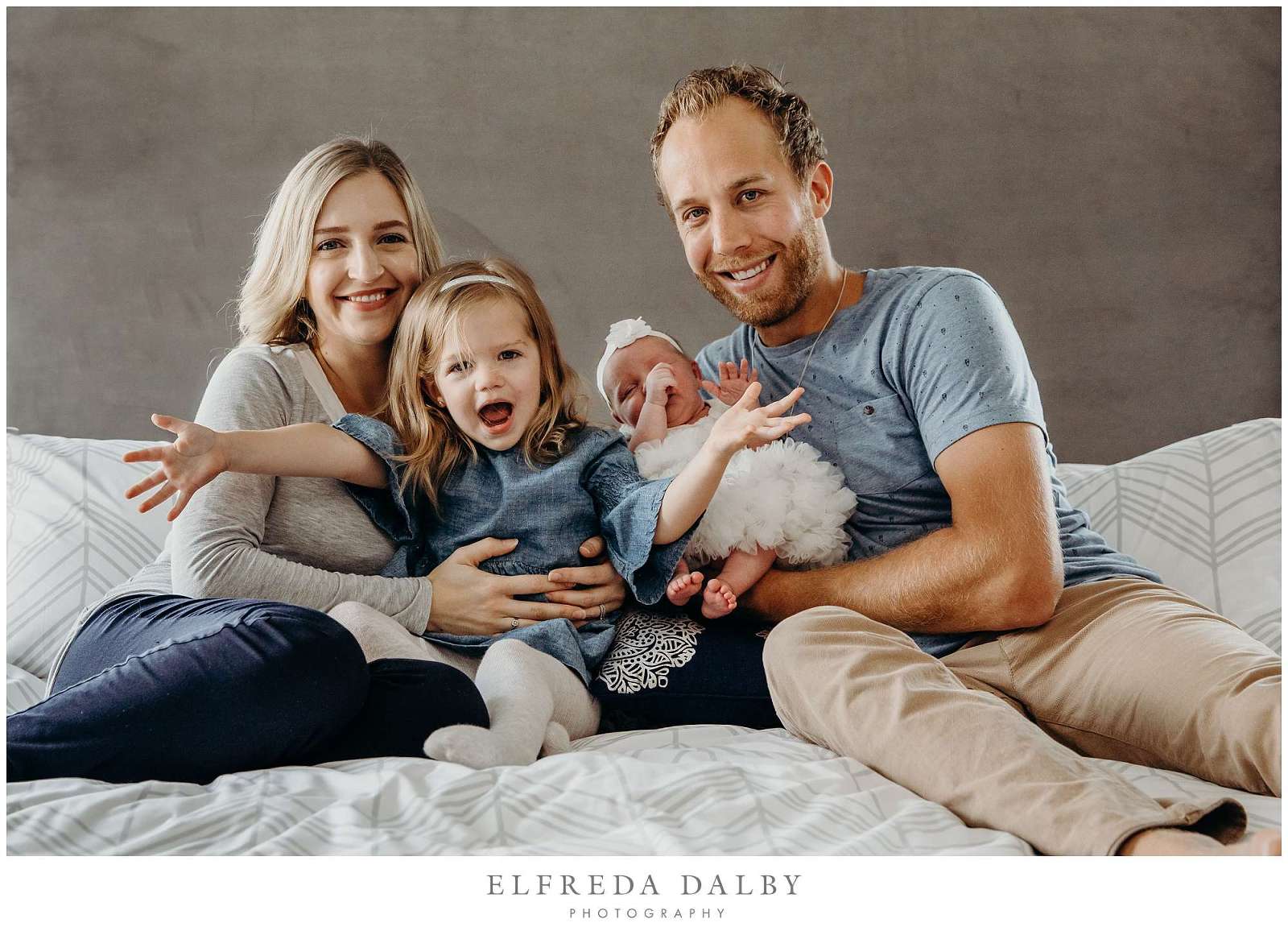 Happy family sitting on a bed with their newborn baby girl