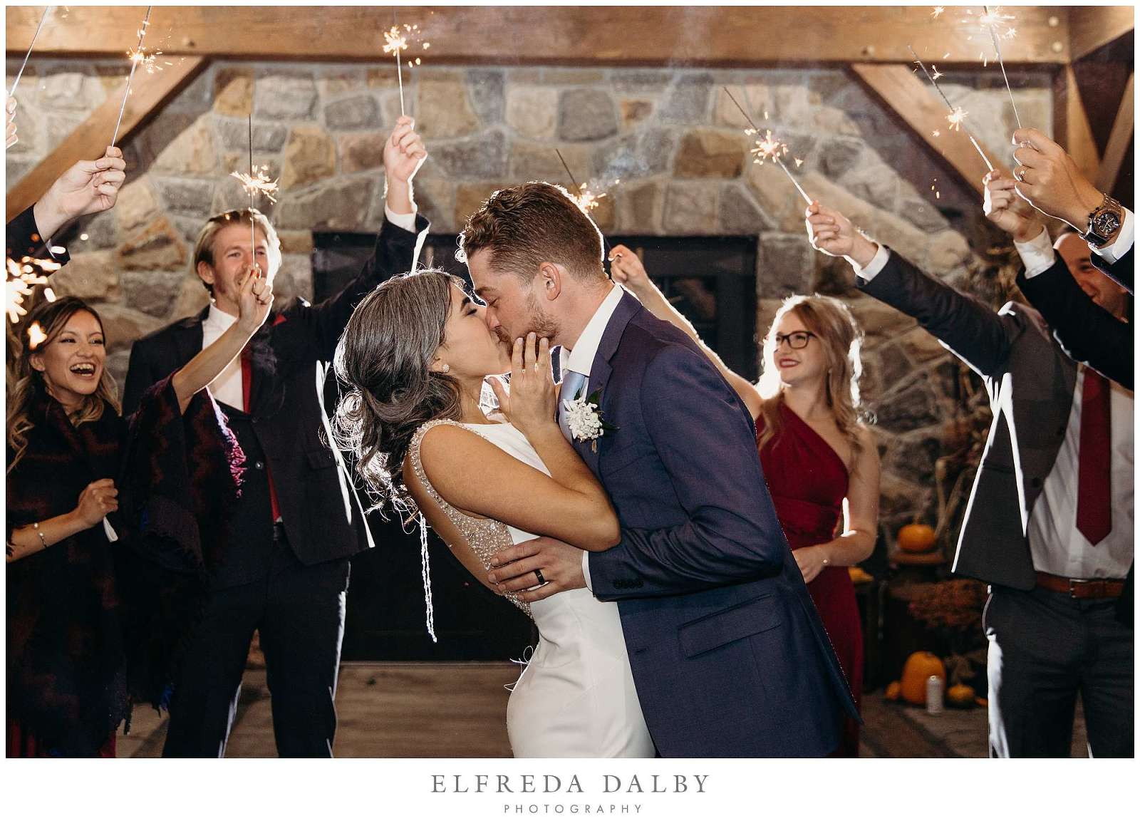 Bride and groom kissing while bridal party holding sparklers