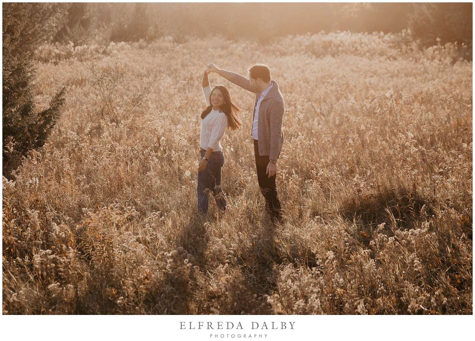 Engaged couple dancing in a field during golden light