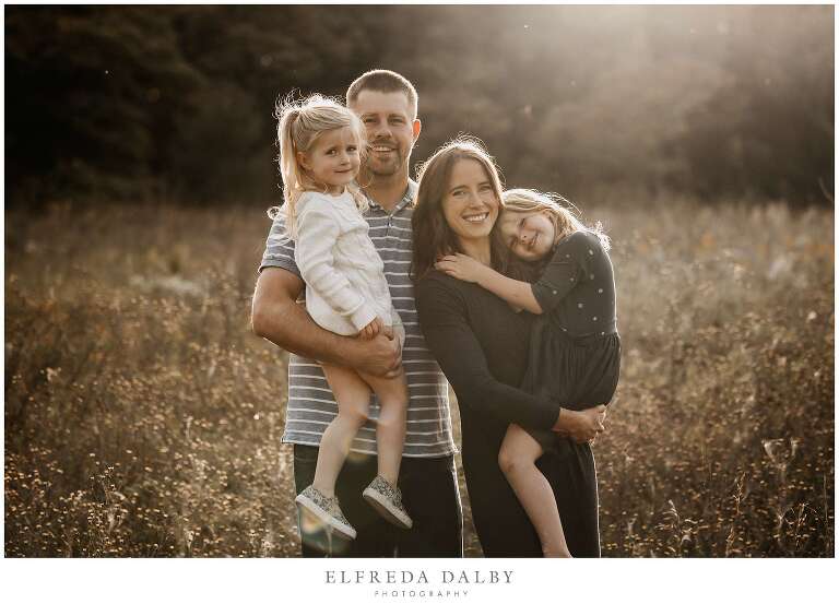 Mother and father with their two girls standing in a field during golden hour