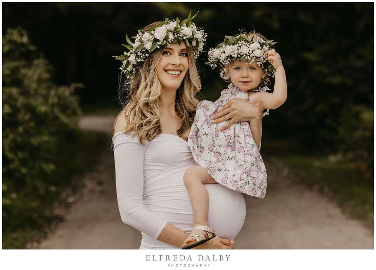 Pregnant mom holding her little girl with flower head pieces