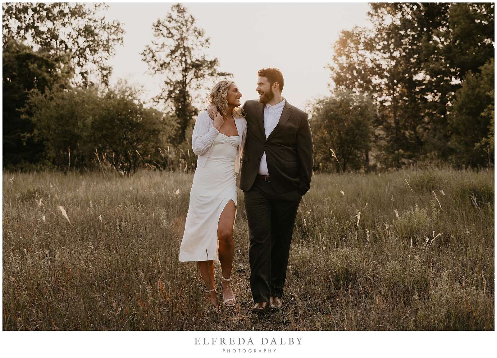 Engaged couple walking in a field during sunset