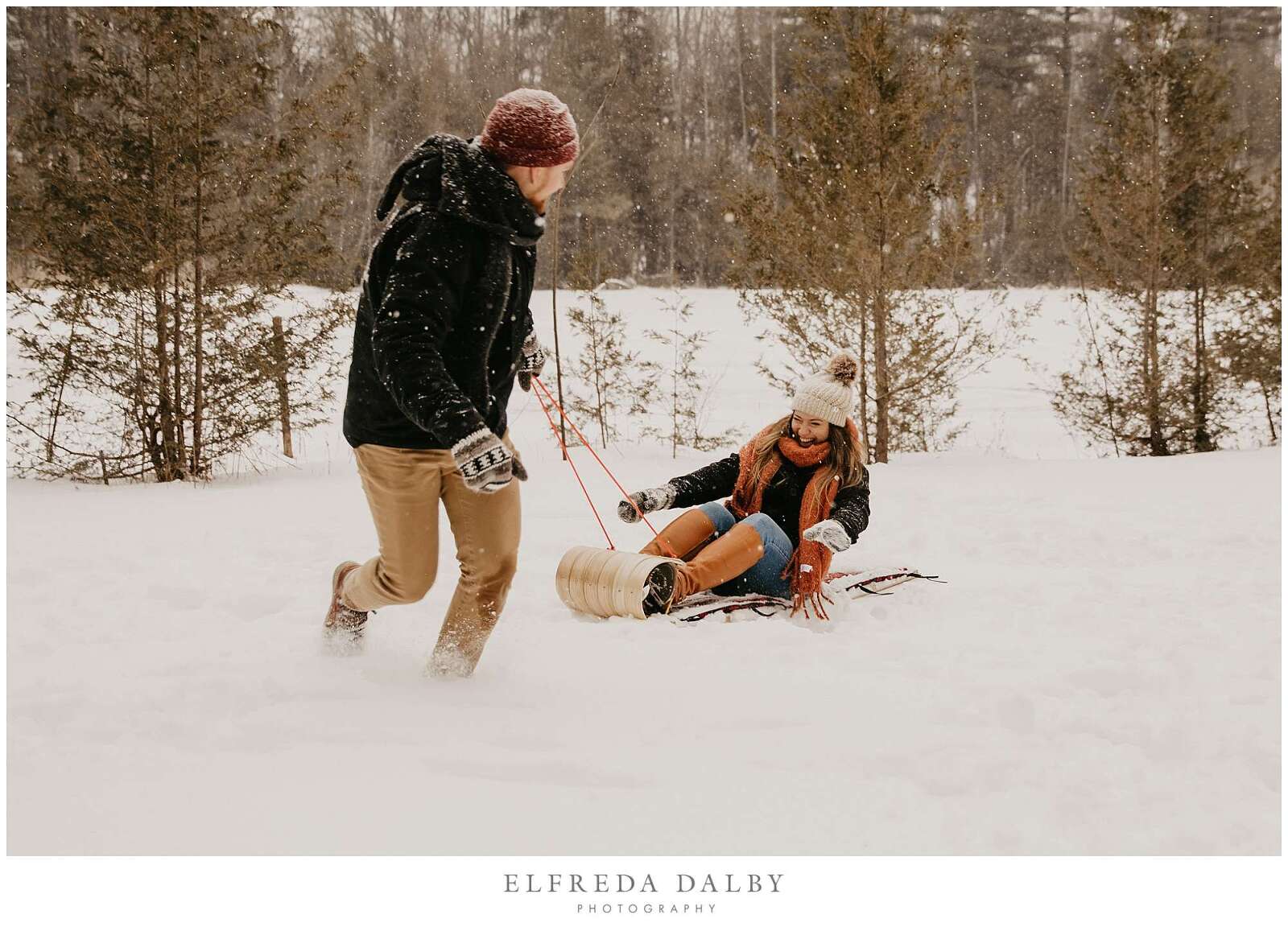 Man pulling his fiancée on a sled through the snow