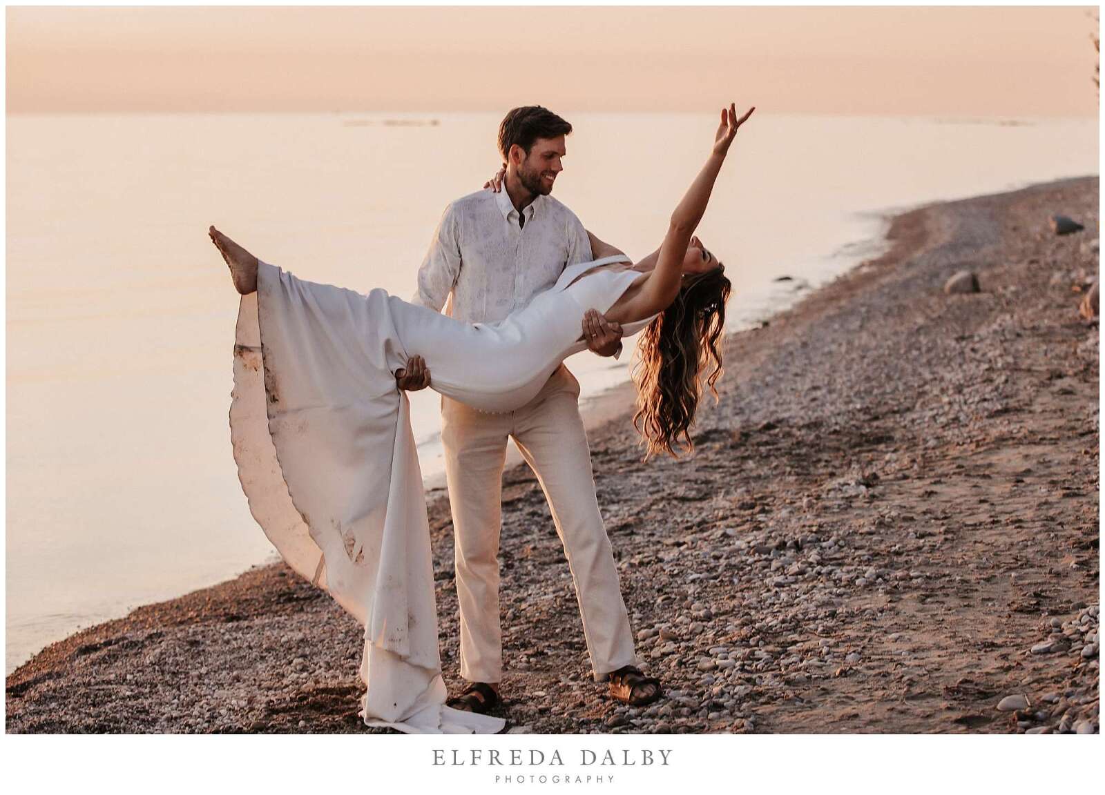 Groom is picking up his bride on the beach during sunset