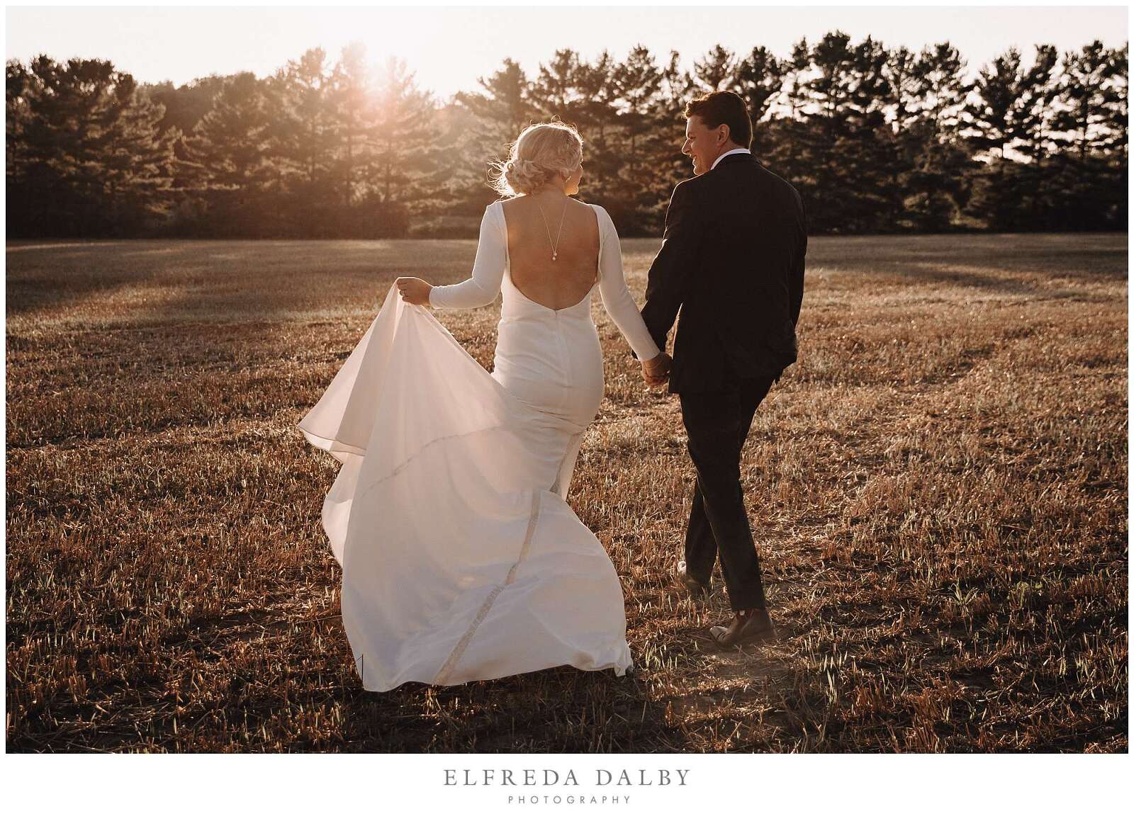 Bride and groom walking away in a farm field at sunset