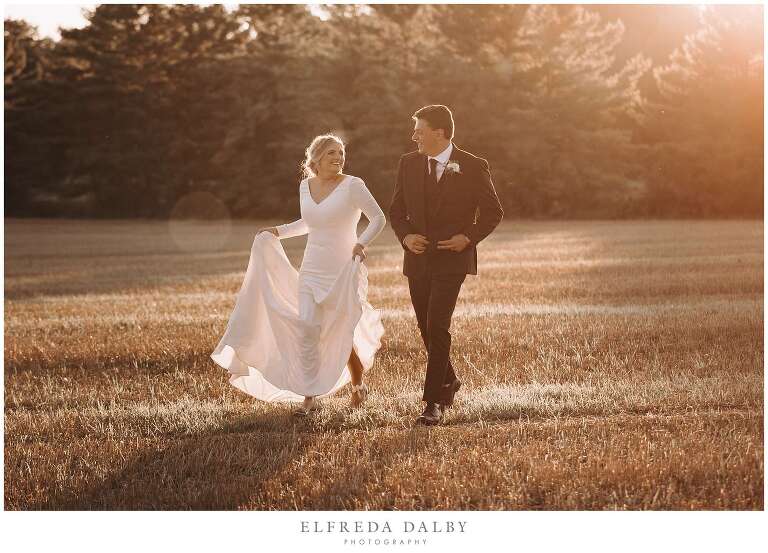 Bride and groom running through a farm field during sunset