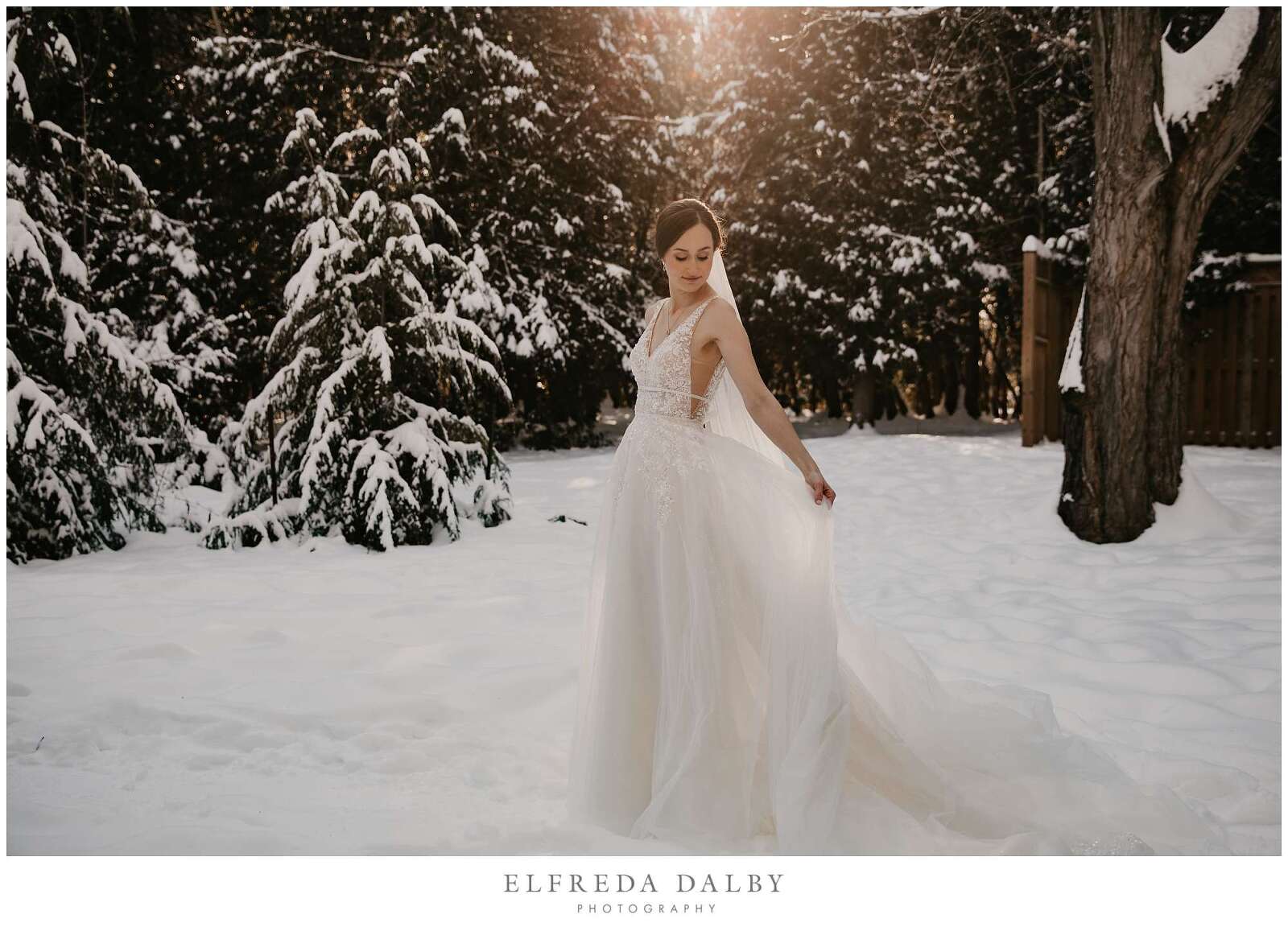 Bride standing in snow with beautiful golden light on her