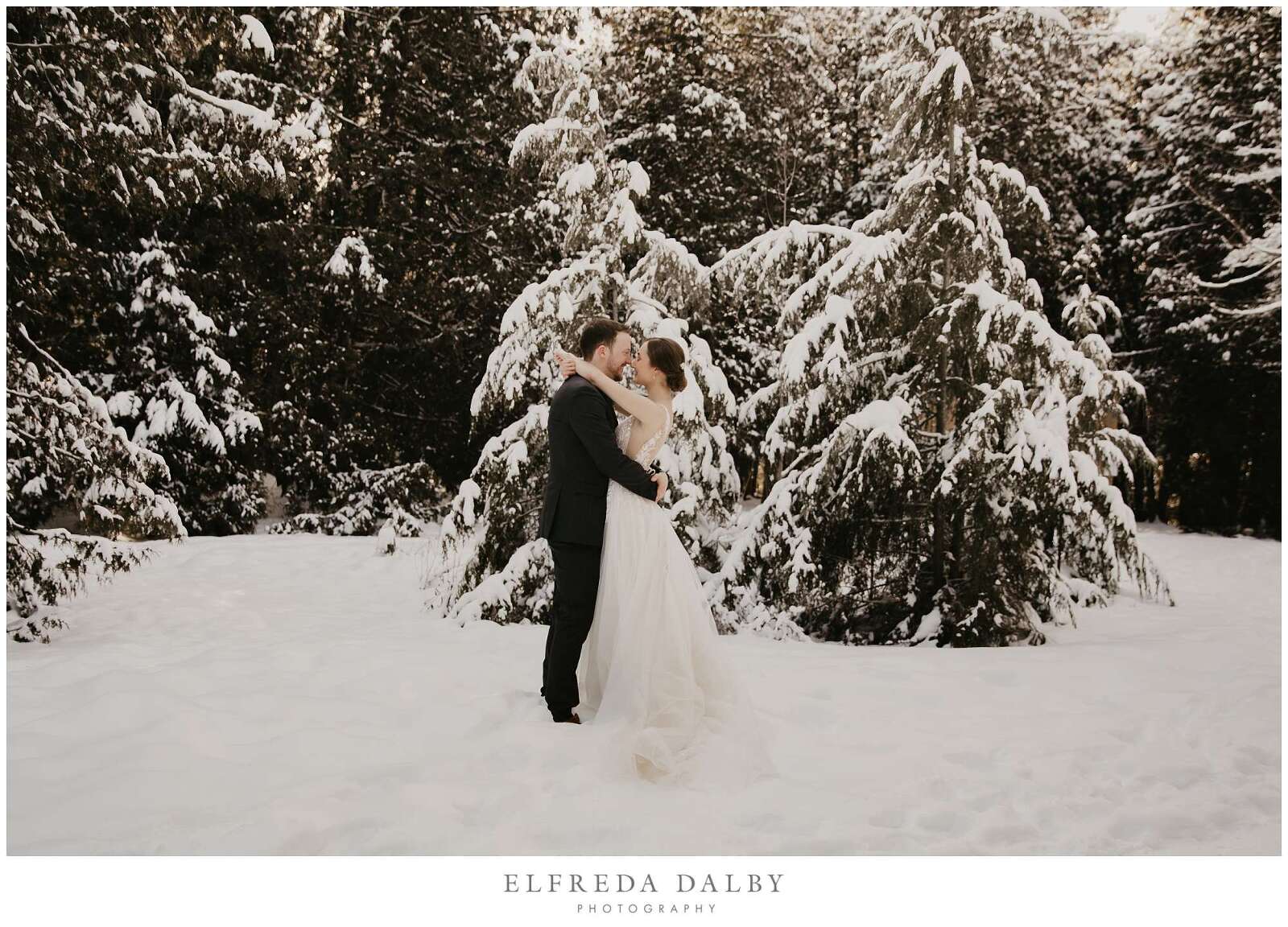 Bride and groom standing in snow during sunset