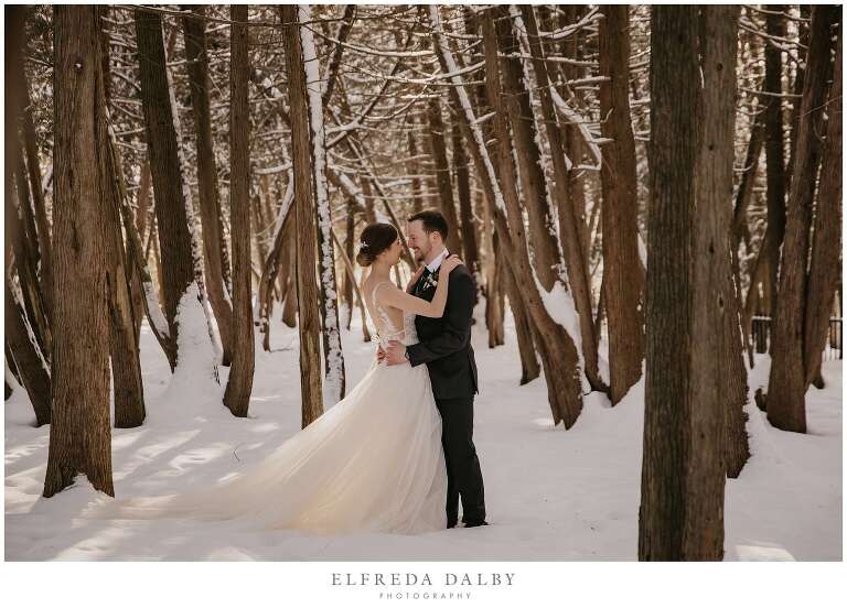 Bride and groom standing in snow in the woods in Elora