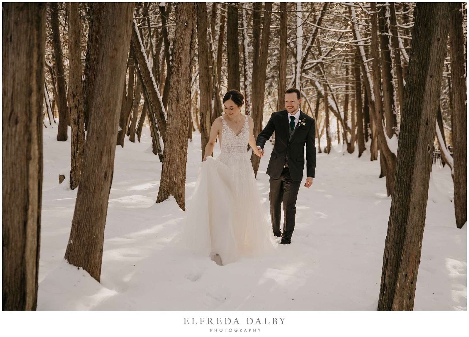 Bride and groom walking through a snowy woods
