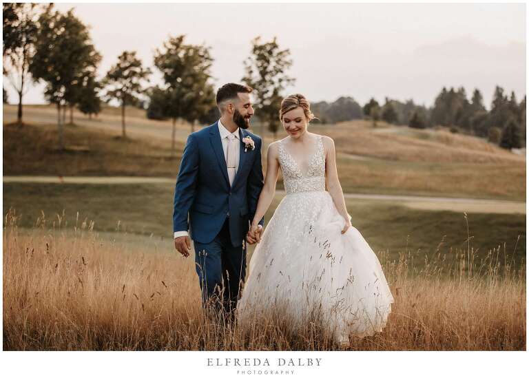 Bride and groom walking through a grassy field at Whistle Bear Golf Club